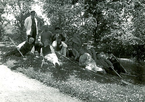 Fotoet viser plejer Skov med et havehold i hospitalsparken omkring 1920. Der holdes pause i skyggen. At der også arbejdes indimellem fremgår ved, at man poserer med sit haveredskab –